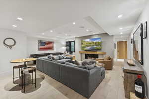 Living room with recessed lighting, light wood finished floors, a glass covered fireplace, and a raised ceiling