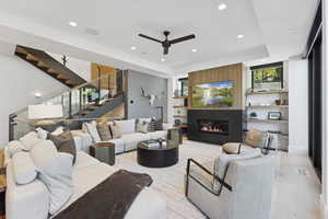 Living area featuring a glass covered fireplace, recessed lighting, ceiling fan, stairway, and a raised ceiling