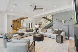 Living room with light wood finished floors, recessed lighting, stairway, and ceiling fan