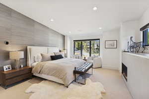 Bedroom with multiple windows, recessed lighting, a warm lit fireplace, light carpet, and an accent wall
