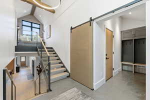 Staircase with a towering ceiling, beam ceiling, a barn door, and recessed lighting