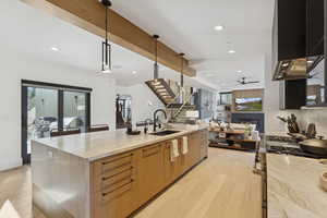 Kitchen featuring light stone counters, stainless steel gas range oven, hanging light fixtures, light wood-style floors, and wall chimney range hood