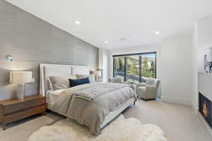 Bedroom featuring an accent wall, a warm lit fireplace, light colored carpet, and recessed lighting