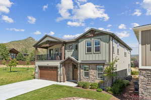 Craftsman house featuring stone siding, concrete driveway, board and batten siding, a front yard, and an attached garage