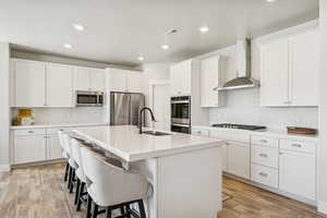 Kitchen with decorative backsplash, wall chimney range hood, stainless steel appliances, a breakfast bar area, and a center island with sink