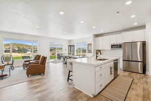 Kitchen with white cabinetry, stainless steel appliances, a kitchen island with sink, a textured ceiling, and light wood-type flooring