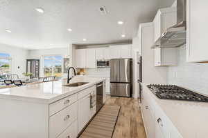 Kitchen with white cabinets, tasteful backsplash, wall chimney exhaust hood, stainless steel appliances, and recessed lighting