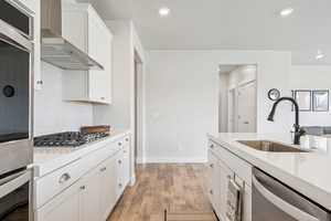 Kitchen with white cabinetry, light wood-type flooring, wall chimney exhaust hood, appliances with stainless steel finishes, and decorative backsplash