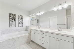 Full bath featuring double vanity, a garden tub, and light marble finish flooring