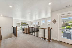 Corridor featuring carpet floors, an upstairs landing, healthy amount of natural light, a textured ceiling, and recessed lighting
