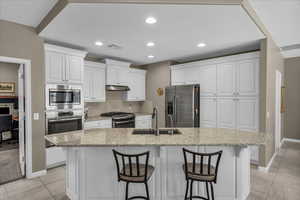 Kitchen with white cabinetry, stainless steel appliances, a kitchen breakfast bar, tasteful backsplash, and light stone counters