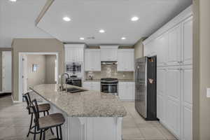 Kitchen with white cabinets, tasteful backsplash, appliances with stainless steel finishes, a kitchen breakfast bar, and a kitchen island with sink
