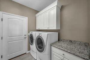 Laundry room featuring light tile patterned floors, cabinet space, separate washer and dryer, and a textured ceiling