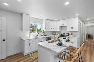 Kitchen featuring white cabinetry, stainless steel appliances, light stone countertops, dark wood finished floors, and recessed lighting