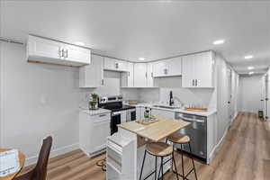 Kitchen with appliances with stainless steel finishes, white cabinets, light wood-style floors, recessed lighting, and light stone counters