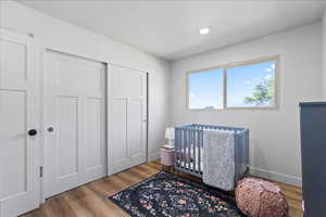 Bedroom with wood finished floors, a crib, a closet, and recessed lighting