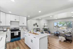 Kitchen with white cabinets, stainless steel electric stove, open floor plan, recessed lighting, and light wood finished floors