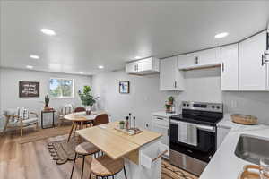 Kitchen with stainless steel electric range oven, white cabinetry, light wood-style flooring, recessed lighting, and light stone countertops