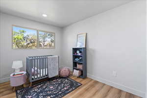 Bedroom with light wood-style flooring, a crib, and recessed lighting