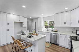 Kitchen with white cabinets, electric range oven, light stone countertops, stainless steel dishwasher, and light wood finished floors