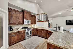 Kitchen featuring stainless steel appliances, a peninsula, light stone countertops, light wood finished floors, and backsplash