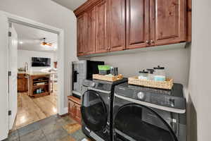 Washroom featuring cabinet space, stone tile floors, separate washer and dryer, and a ceiling fan