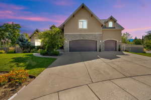View of front of property with stone siding, an attached garage, stucco siding, and concrete driveway
