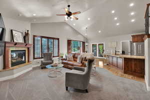 Living room featuring a fireplace, high vaulted ceiling, recessed lighting, a ceiling fan, and light colored carpet
