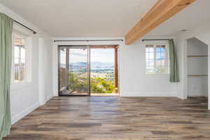 Unfurnished room with plenty of natural light, wood finished floors, beamed ceiling, a mountain view, and a textured ceiling