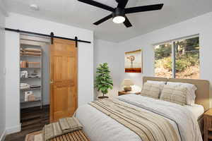 Bedroom with a barn door, wood finished floors, ceiling fan, and a textured ceiling (Virtually staged)