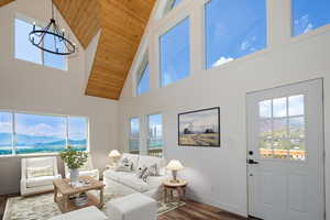 Living room with a mountain view, dark wood-style flooring, wooden ceiling, high vaulted ceiling, and plenty of natural light (Virtually staged)