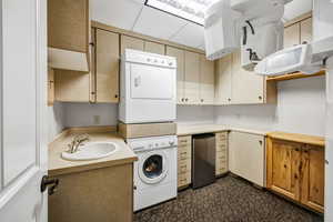Breakroom with light countertops, stacked washer / drying machine and wood cabinets with dark colored carpet