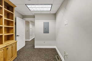 Office with a paneled ceiling, dark colored carpet, and electric panel