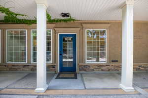 Doorway to property featuring stone siding, a porch, and stucco siding