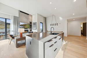 Kitchen featuring modern cabinets, light wood-style flooring, a large fireplace, a center island with sink, and recessed lighting