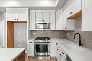 Kitchen with appliances with stainless steel finishes, decorative backsplash, white cabinetry, light stone countertops, and light wood-style floors