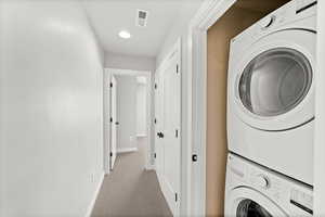 Laundry room with carpet floors, stacked washer and clothes dryer, and recessed lighting