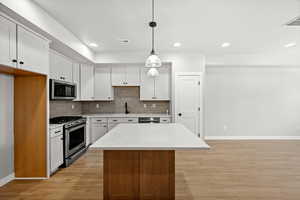 Kitchen featuring white cabinetry, backsplash, appliances with stainless steel finishes, decorative light fixtures, and a center island