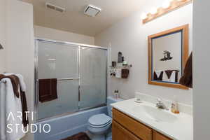 Full bathroom featuring vanity, combined bath / shower with glass door, and a textured ceiling