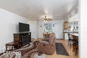 Living room with light wood finished floors, a ceiling fan, and a textured ceiling