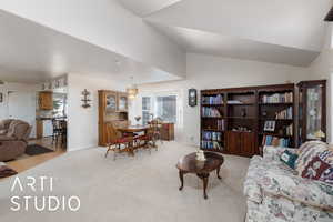 Living area featuring light carpet, a chandelier, and vaulted ceiling
