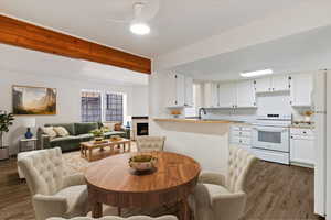 Dining area with dark wood-type flooring, beam ceiling, a warm lit fireplace, and ceiling fan