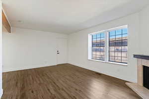 Unfurnished living room featuring dark wood finished floors, a tile fireplace, beamed ceiling, and a textured ceiling