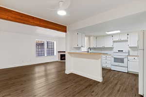 Kitchen with white appliances, white cabinetry, light countertops, open floor plan, and beam ceiling