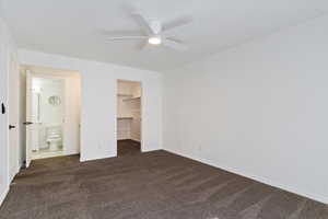 Unfurnished bedroom with dark colored carpet, a walk in closet, and a ceiling fan