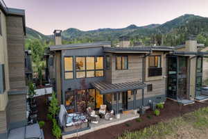 Back of property at dusk with a chimney, a mountain view, and a patio area