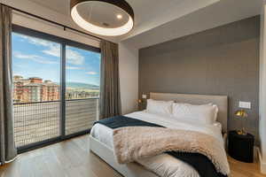 Bedroom with wood finished floors, an accent wall, access to outside, and wallpapered walls