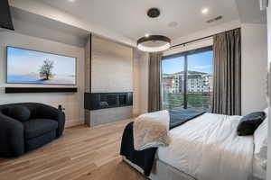 Bedroom with light wood finished floors, a multi sided fireplace, and recessed lighting