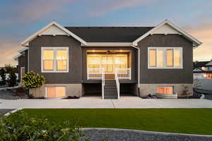 Back of house at dusk with a yard, ceiling fan, stucco siding, and covered porch