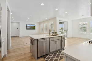 Kitchen featuring light wood-style floors, stainless steel dishwasher, recessed lighting, a center island with sink, and hanging light fixtures, looking into the famlyroom.